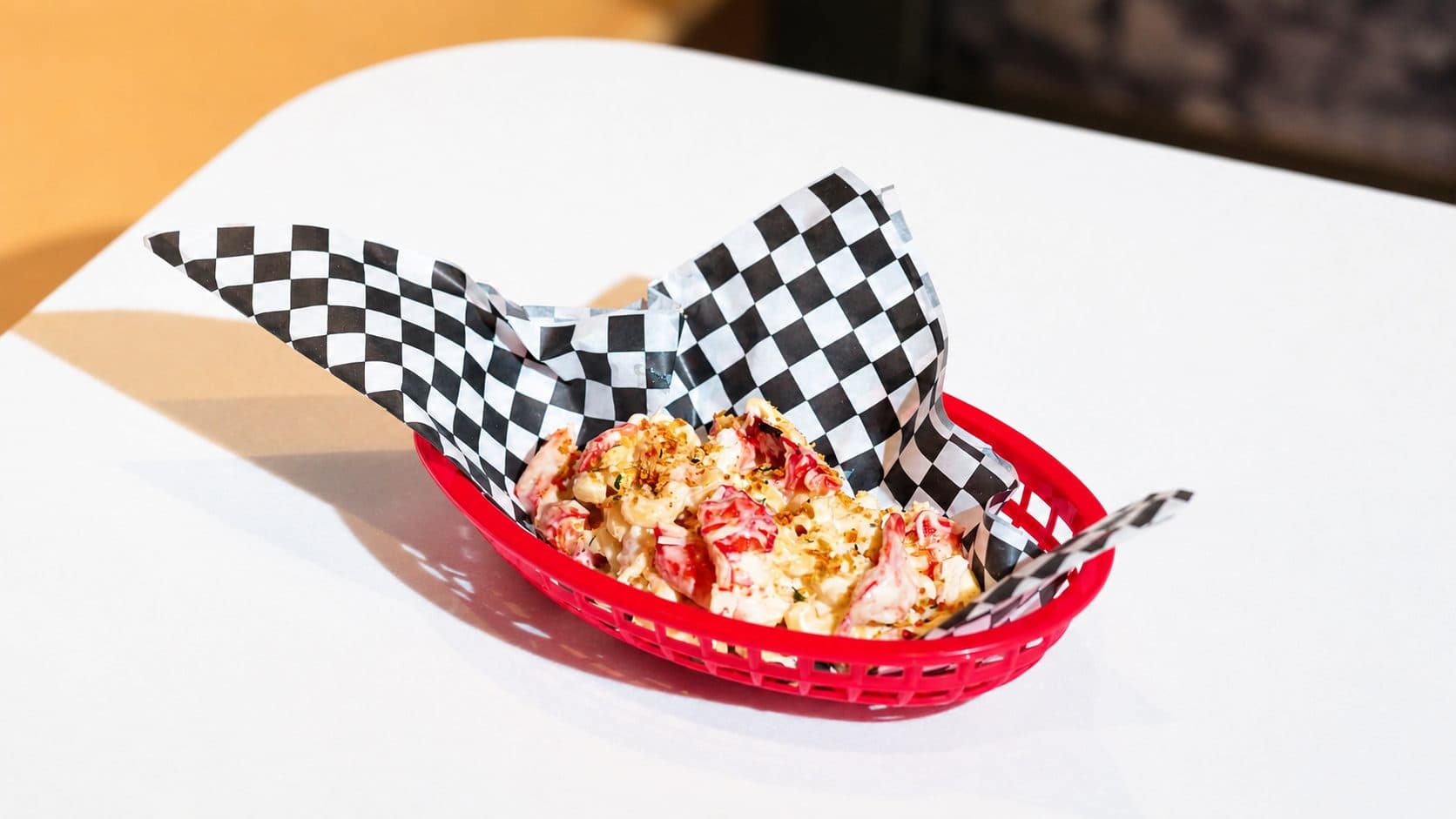 Lobster mac and cheese, macaroni in a cream sauce with lobster meat and a crumb topping, in a red basket lined with black and white checked paper.